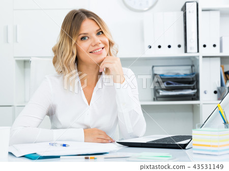 Smiling girl in white shirt sitting at office desk in well-lit office 43531149