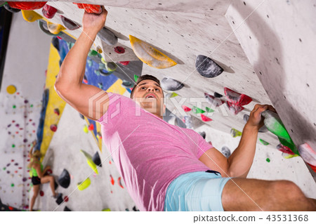 Male alpinist practicing indoor rock-climbing on artificial boulder without safety belts Male alpinist practicing indoor rock-climbing on artificial boulder without safety belts 43531368
