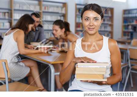 Smiling girl with pile of books in library Smiling girl with pile of books in library 43531531