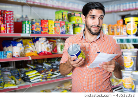 Adult man is choosing conserved peas with help note list in market. 43532358