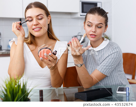 Two positive young female friend doing make up at table with cosmetics Two positive young female friend doing make up at table with cosmetics 43532674