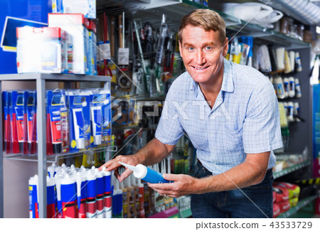 Portrait of male customer selecting sealant bottle i 43533729