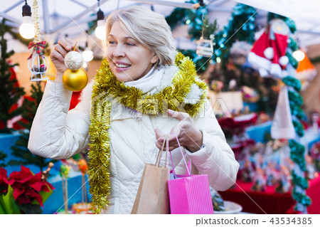 Positive mature female buying decoration at Christmas Fair Positive mature female buying decoration at Christmas Fair 43534385