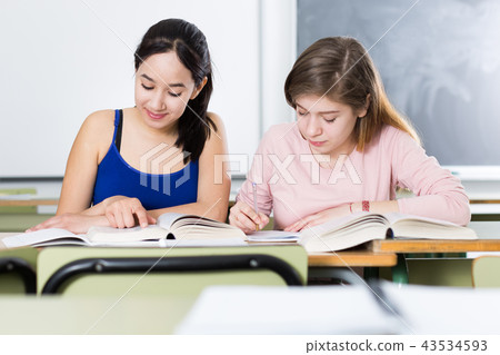 Two girls are sitting at the desk and writing homework Two girls are sitting at the desk and writing homework 43534593