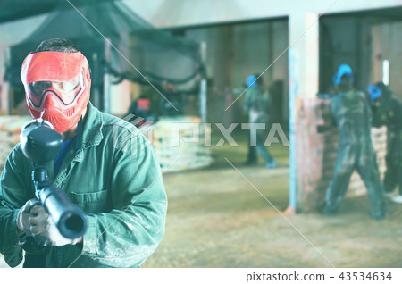 Portrait of red team player who is aiming in opponents on paintball field. Portrait of red team player who is aiming in opponents on paintball field. 43534634