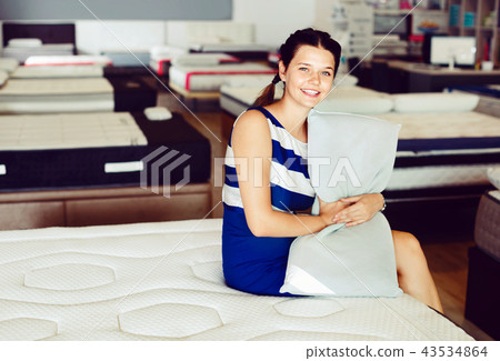 Young woman is sitting on bed with new pillow in the store. Young woman is sitting on bed with new pillow in the store. 43534864