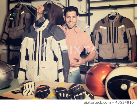 Man is demonstrating new jacket for motorbike in the store. 43534910