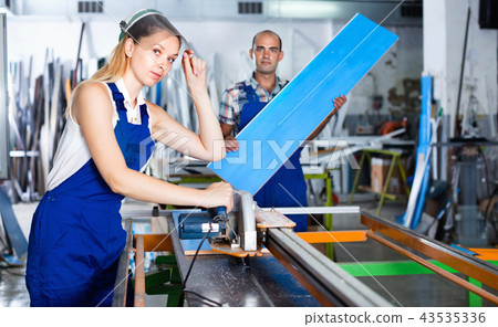 Female worker in protective face shield, standing near circular saw 43535336