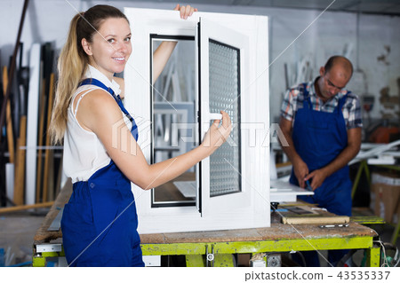 Positive woman in blue overalls demonstrating pvc window Positive woman in blue overalls demonstrating pvc window 43535337
