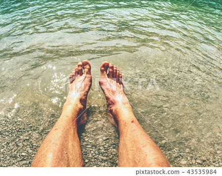 Legs in wave of water and rough white stony sand 43535984
