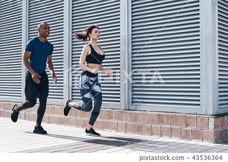 Urban sports. Full length of young couple in sport clothing running through the city street together 43536364