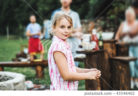 A small girl standing outdoors on a barbecue grill party in the backyard. 43546402