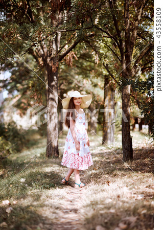 a girl with wide hat walks along a forest path 43558109