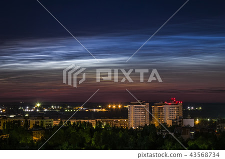 Night sky view of beautiful noctilucent clouds over the city with a cityscape at foreground. 43568734