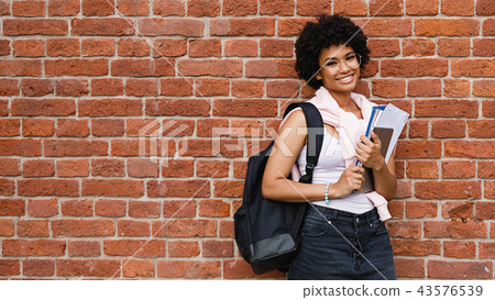 Happy female student with books standing at wall 43576539
