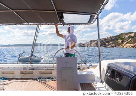 Attractive male skipper navigating the fancy catamaran sailboat on sunny summer day on calm blue sea 43584395