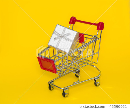 Shopping trolley with silver gift on a yellow background. Shopping trolley with silver gift on a yellow background. 43590931