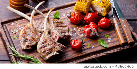 Lamb ribs grilled on cutting board with roasted vegetables. Wooden background. Lamb ribs grilled on cutting board with roasted vegetables. Wooden background. 43605466