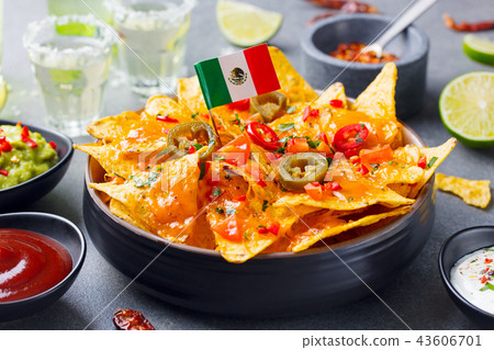 Nachos chips with Mexican flag and dips variety in black bowl. Grey stone background. Nachos chips with Mexican flag and dips variety in black bowl. Grey stone background. 43606701