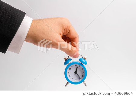 A businessman's hand holds a blue alarm clock 43609664