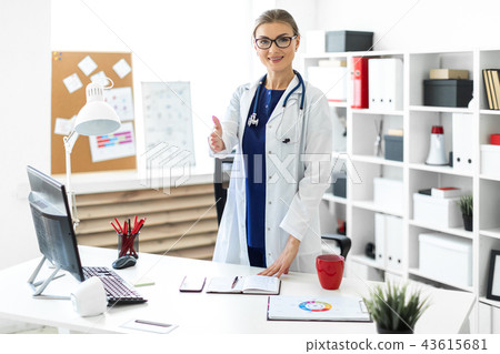 A young girl in a white robe stands near the desk in the office and stretches her right hand forward A young girl in a white robe stands near the desk in the office and stretches her right hand forward 43615681