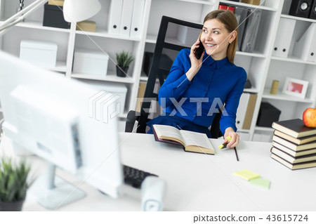 A young girl is sitting at a computer desk, holding a yellow marker in her hand and talking on the 43615724