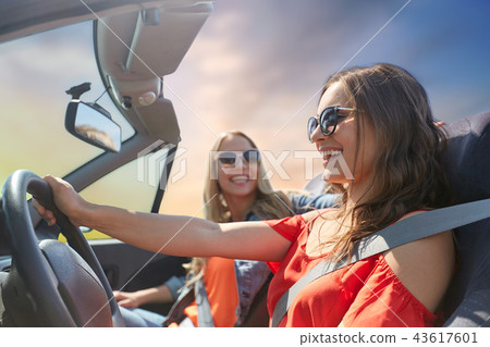 happy young women driving in convertible car 43617601