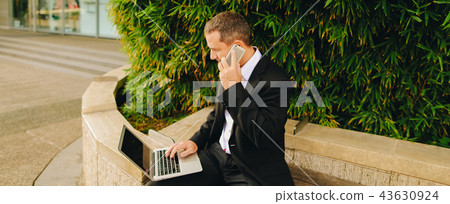 Manager talking by smartphone and working with laptop outside in Manager talking by smartphone and working with laptop outside in 43630924