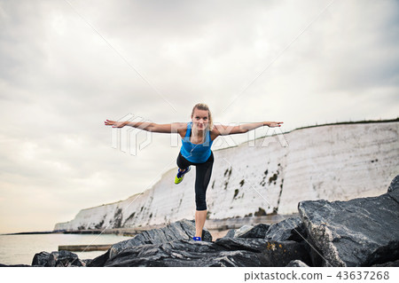 Young sporty woman runner with earphones stretching on the beach outside. 43637268