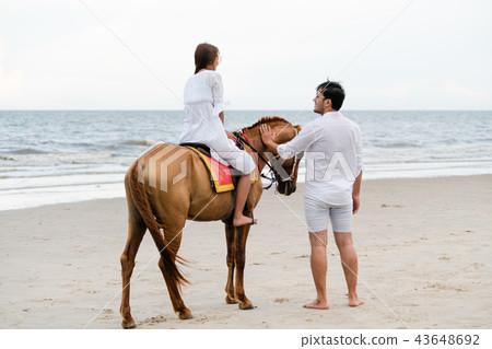 Young couple goes horse riding on tropical beach. 43648692