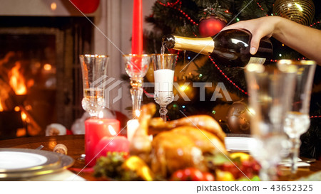 Closeup image of hand filling glasses with champagne on Christmas dining table Closeup image of hand filling glasses with champagne on Christmas dining table 43652325
