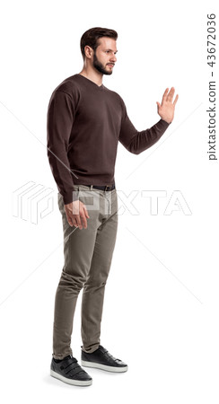 A young bearded man in a side view stands with one hand up and held palm to the front. 43672036