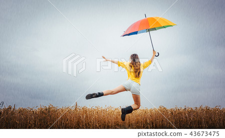 Woman jumping with colorful umbrella in the rain 43673475