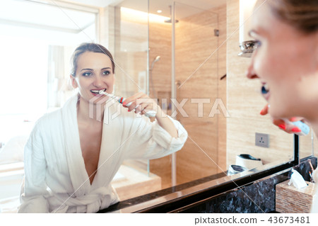 Woman brushing her teeth in luxurious hotel looking at herself Woman brushing her teeth in luxurious hotel looking at herself 43673481