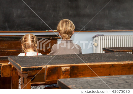 Concept of public primary school education with young boy and girl sitting in the classroom 43675080
