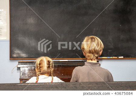 Concept of public primary school education with young boy and girl sitting in the classroom 43675084