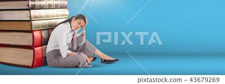 Business woman sitting next to a pile of books on blue background 43679269