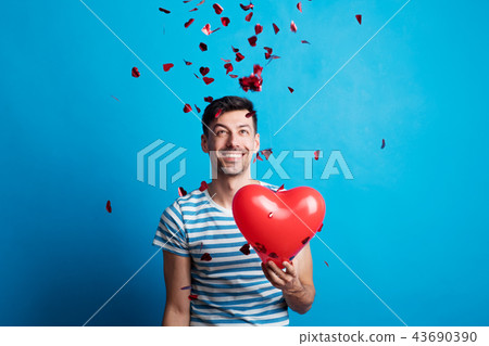 A young man in love holding red heart, confetti falling on him. 43690390