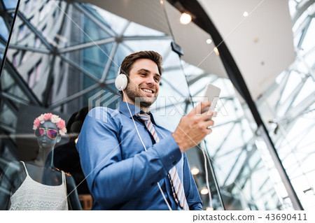 A young businessman with smartphone and headphones in a modern building. 43690411