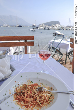 spaghetti and wine glass on table by sea spaghetti and wine glass on table by sea 43694075