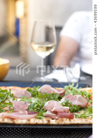 Italian pizza with arugula and ham. A delicious traditional meal for lunch and a glass of white wine Italian pizza with arugula and ham. A delicious traditional meal for lunch and a glass of white wine 43699599