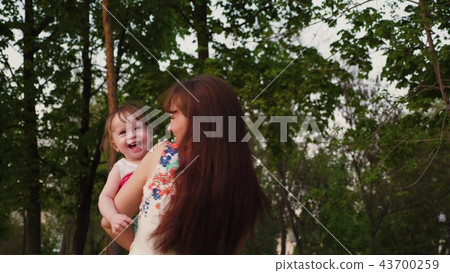 Young mother plays in the park with a small baby laughing and shaking it in her arms. Young mother plays in the park with a small baby laughing and shaking it in her arms. 43700259