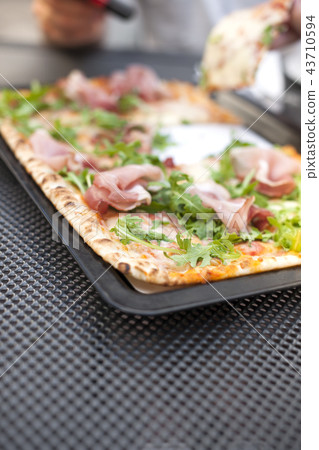Italian pizza with arugula and ham. Delicious traditional food for lunch. Homemade baking. Top view. Italian pizza with arugula and ham. Delicious traditional food for lunch. Homemade baking. Top view. 43710594