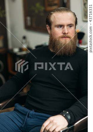 Handsome young bearded guy sitting in an armchair in a beauty salon Handsome young bearded guy sitting in an armchair in a beauty salon 43716331