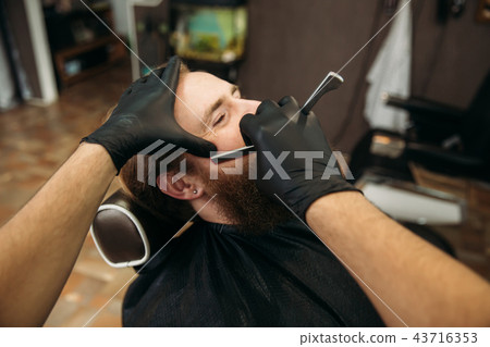 Bearded man with long beard getting stylish hair shaving , haircut , with razor by barber in Bearded man with long beard getting stylish hair shaving , haircut , with razor by barber in 43716353