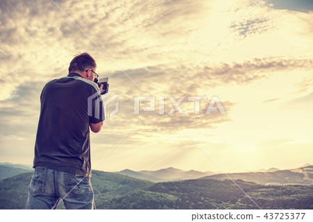 Man taking picture of landscape awaking in mist Man taking picture of landscape awaking in mist 43725377