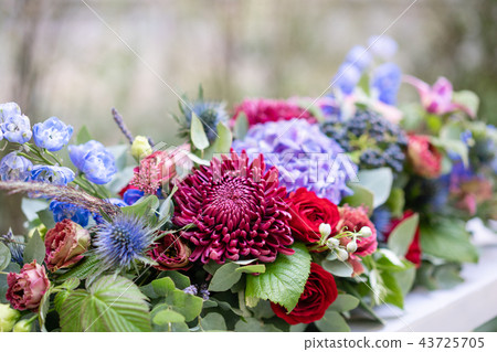 Elongated floral arrangement in vintage metal vase. table setting. Blue and red color. Gorgeous Elongated floral arrangement in vintage metal vase. table setting. Blue and red color. Gorgeous 43725705