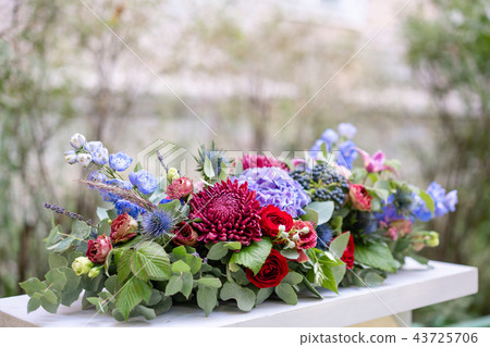 Elongated floral arrangement in vintage metal vase. table setting. Blue and red color. Gorgeous 43725706