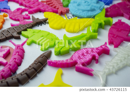 Many bright multi-colored objects printed on 3d printer lie on flat surface Many bright multi-colored objects printed on 3d printer lie on flat surface 43726115