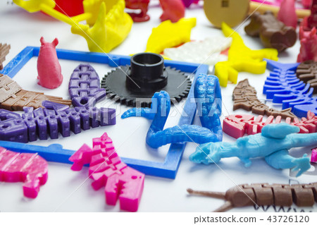 Many bright multi-colored objects printed on 3d printer lie on flat surface Many bright multi-colored objects printed on 3d printer lie on flat surface 43726120